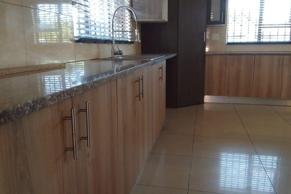 Modern kitchen featuring light wood-finish cabinetry, granite countertops, stainless steel sink, and tiled flooring with ample natural light.