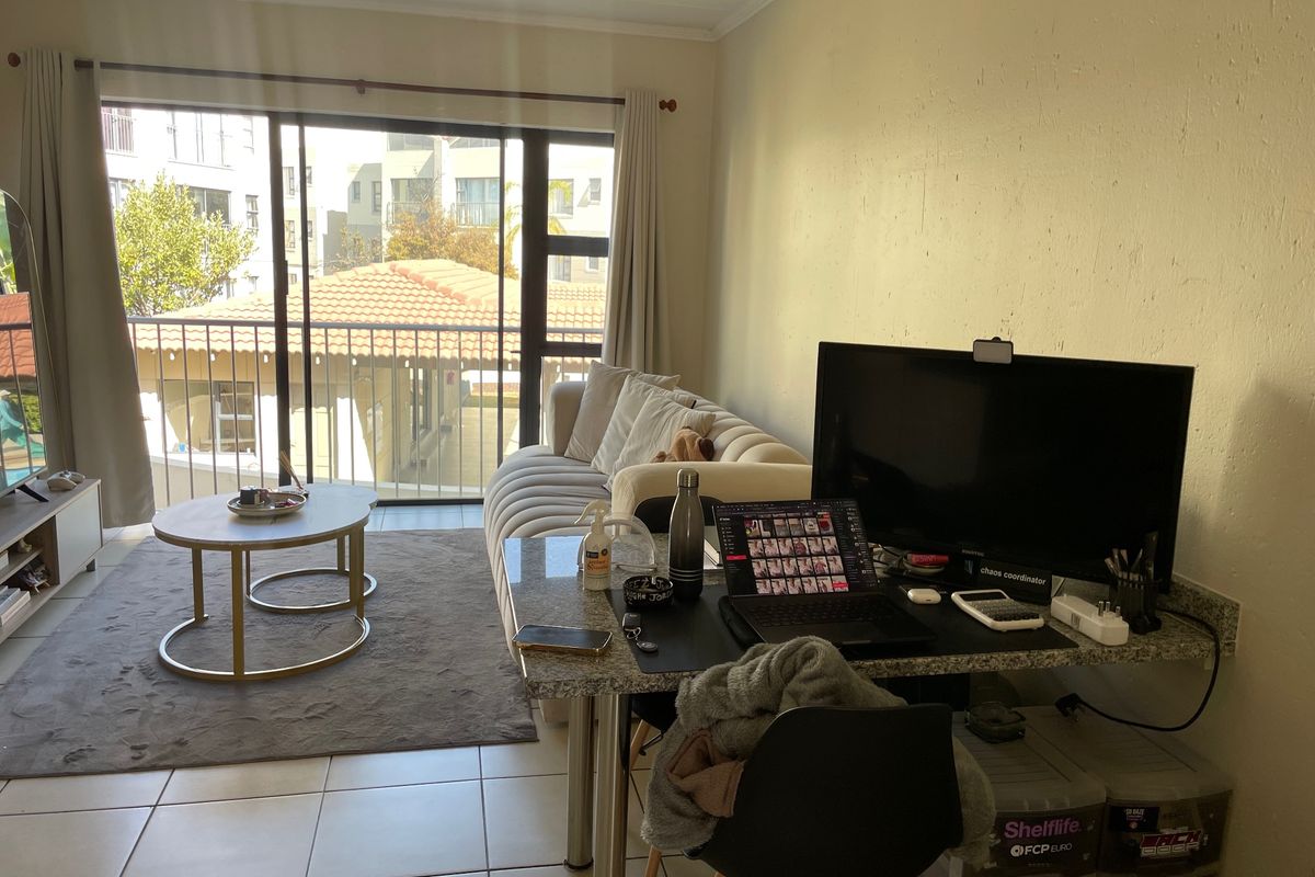 A living room area featuring tiled floors, a built-in granite desk space, and a sliding glass door leading to a balcony.
