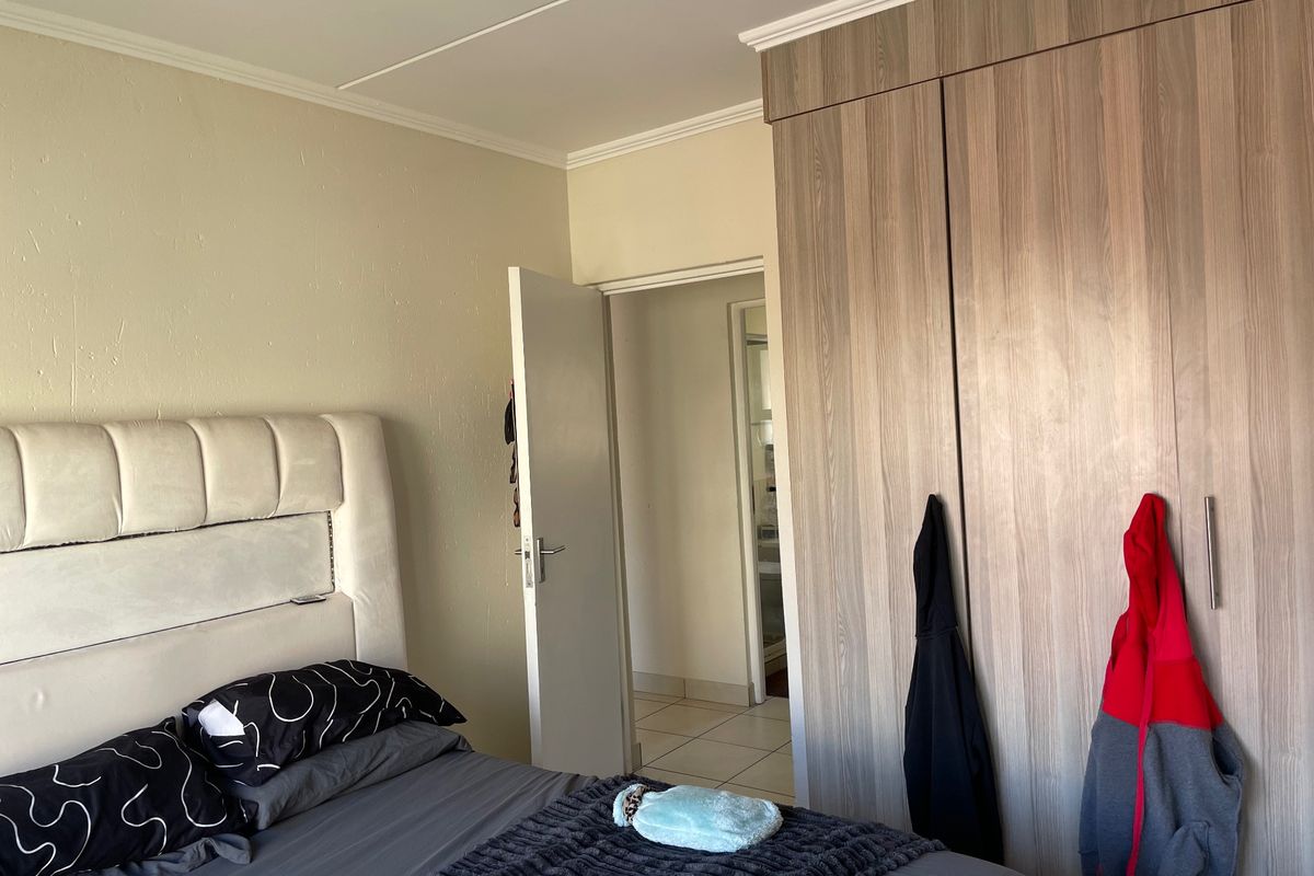 A bedroom featuring a built-in wooden wardrobe and crown molding, with an adjacent doorway leading to a tiled hallway.
