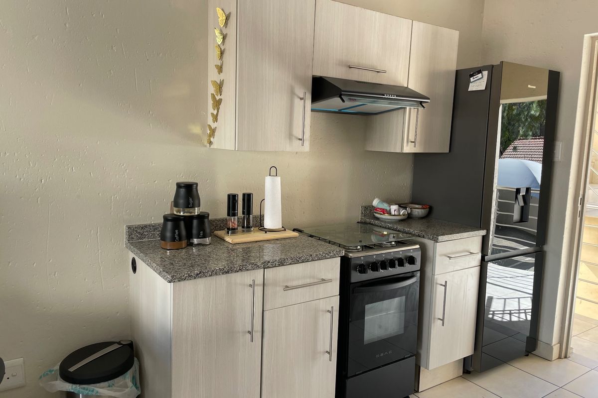 A compact kitchen featuring light wood-grain cabinetry, granite countertops, and a freestanding stove with an integrated extractor fan.