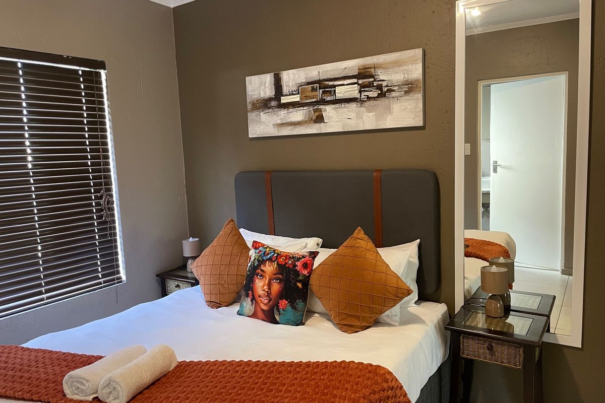 A cozy bedroom featuring a neutral color palette, venetian blinds for privacy, and a full-length mirror, creating a comfortable and functional sleeping space.