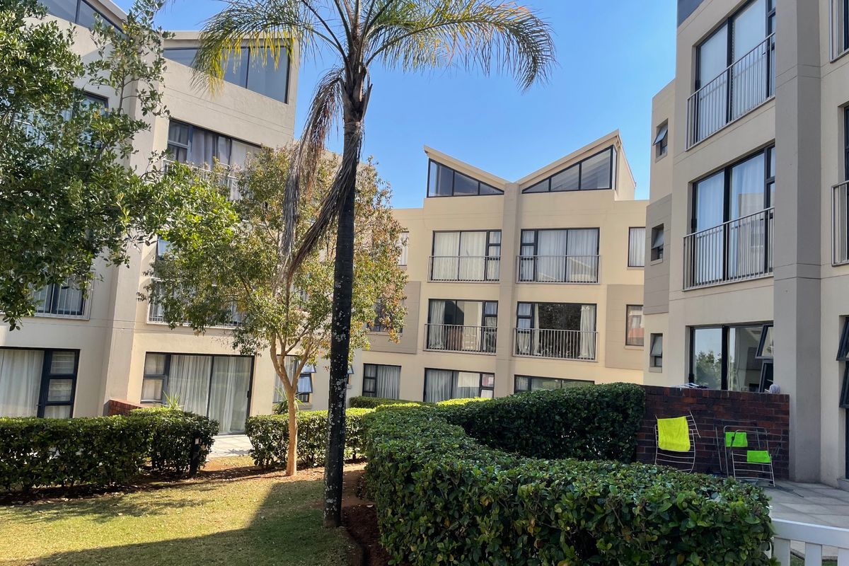 A view of the apartment complex exterior featuring landscaped gardens, paved areas, and multi-story residential units with balconies and large windows.