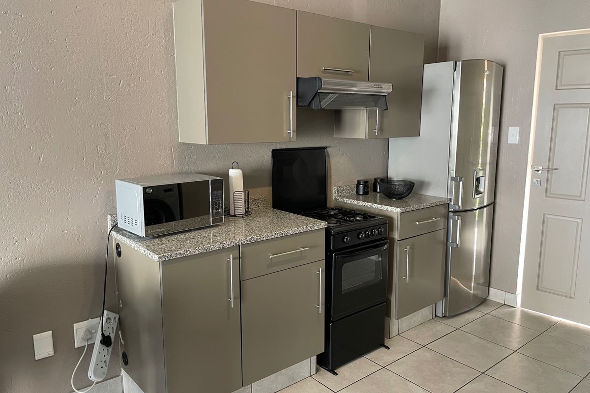 A compact kitchen featuring modern taupe cabinetry, granite countertops, tiled flooring, and a built-in extractor fan.
