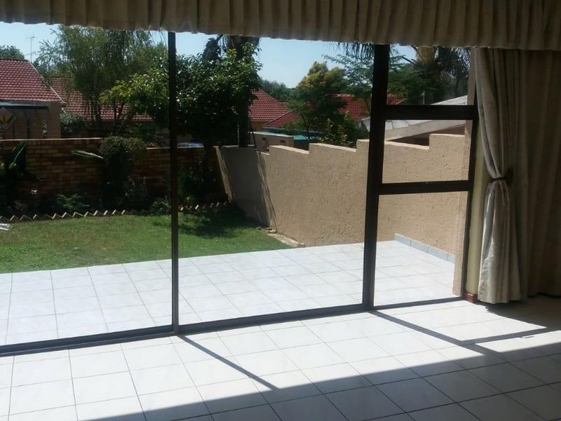A tiled patio area accessible through large sliding glass doors, overlooking a private garden with a perimeter boundary wall.