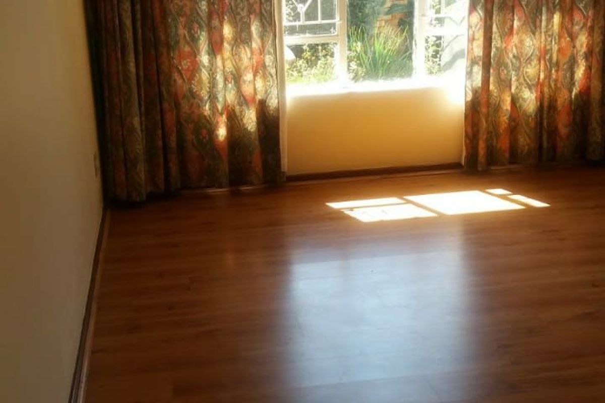 A bright, empty living room featuring warm-toned laminate flooring and a large window with existing curtain tracks, offering a blank canvas for interior design.