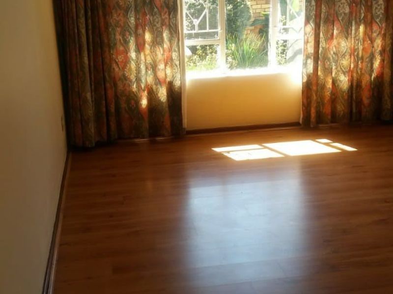 A bright, empty living room featuring warm-toned laminate flooring and a large window with existing curtain tracks, offering a blank canvas for interior design.