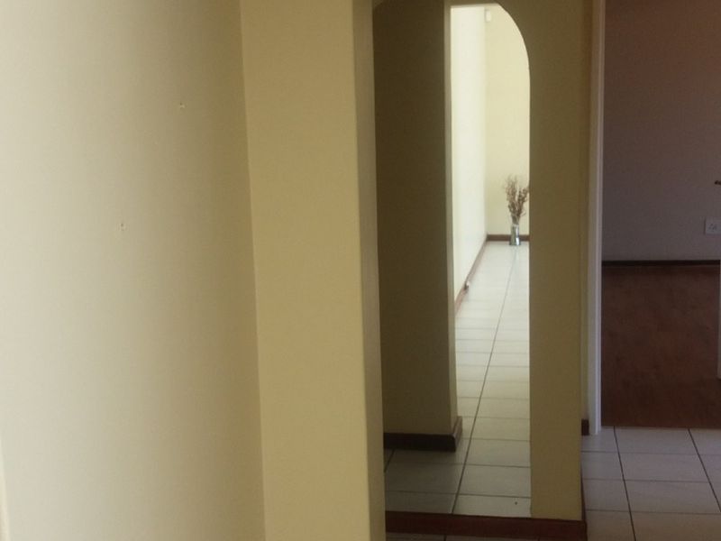 A neutral-toned hallway featuring tiled flooring and a distinctive architectural archway leading to adjacent living spaces.