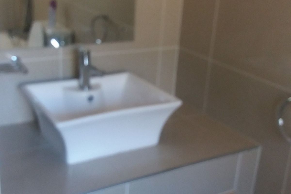 A modern bathroom vanity featuring a white vessel sink, chrome faucet, and open shelving storage with neutral wall tiling.