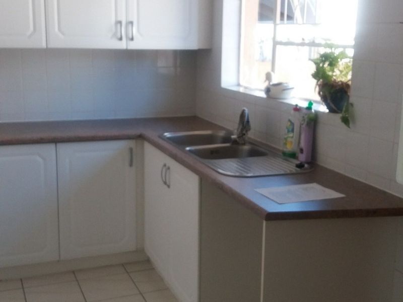 A functional kitchen featuring white cabinetry, laminate countertops, a double bowl stainless steel sink, and tiled flooring with a window providing natural light.