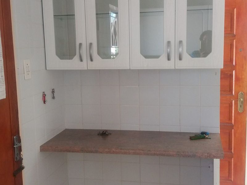 A functional scullery or utility area featuring white glass-fronted wall cabinets, laminate countertop, and tiled finishes, ready for customization.