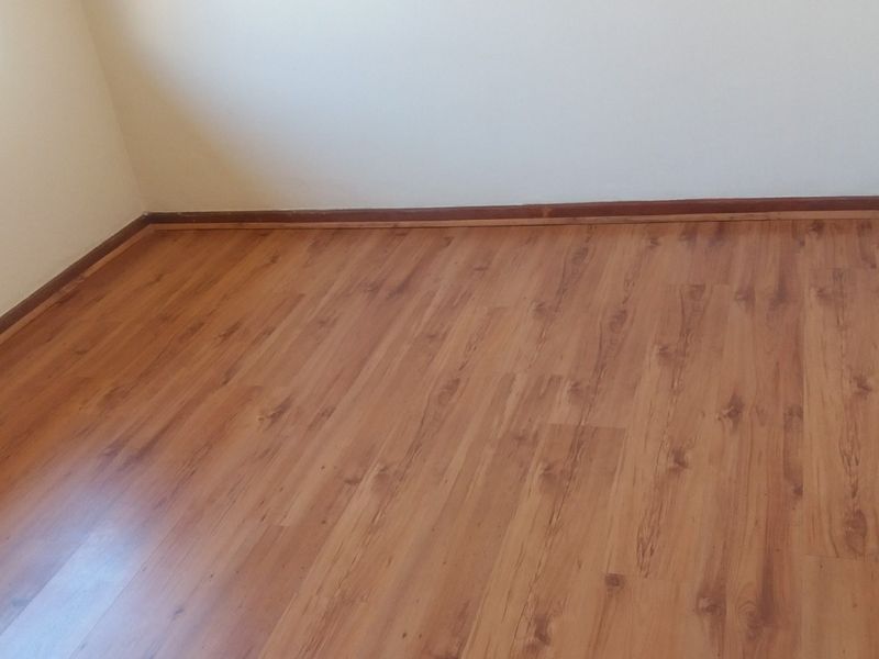 An empty bedroom featuring warm-toned laminate flooring and neutral wall finishes, providing a clean and versatile space ready for personalization.