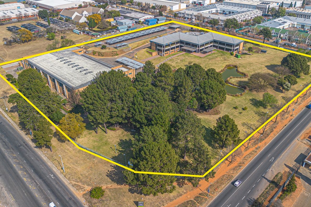 Aerial view of a large commercial property featuring office buildings, a warehouse, extensive landscaped grounds, an ornamental pond, and ample parking facilities.