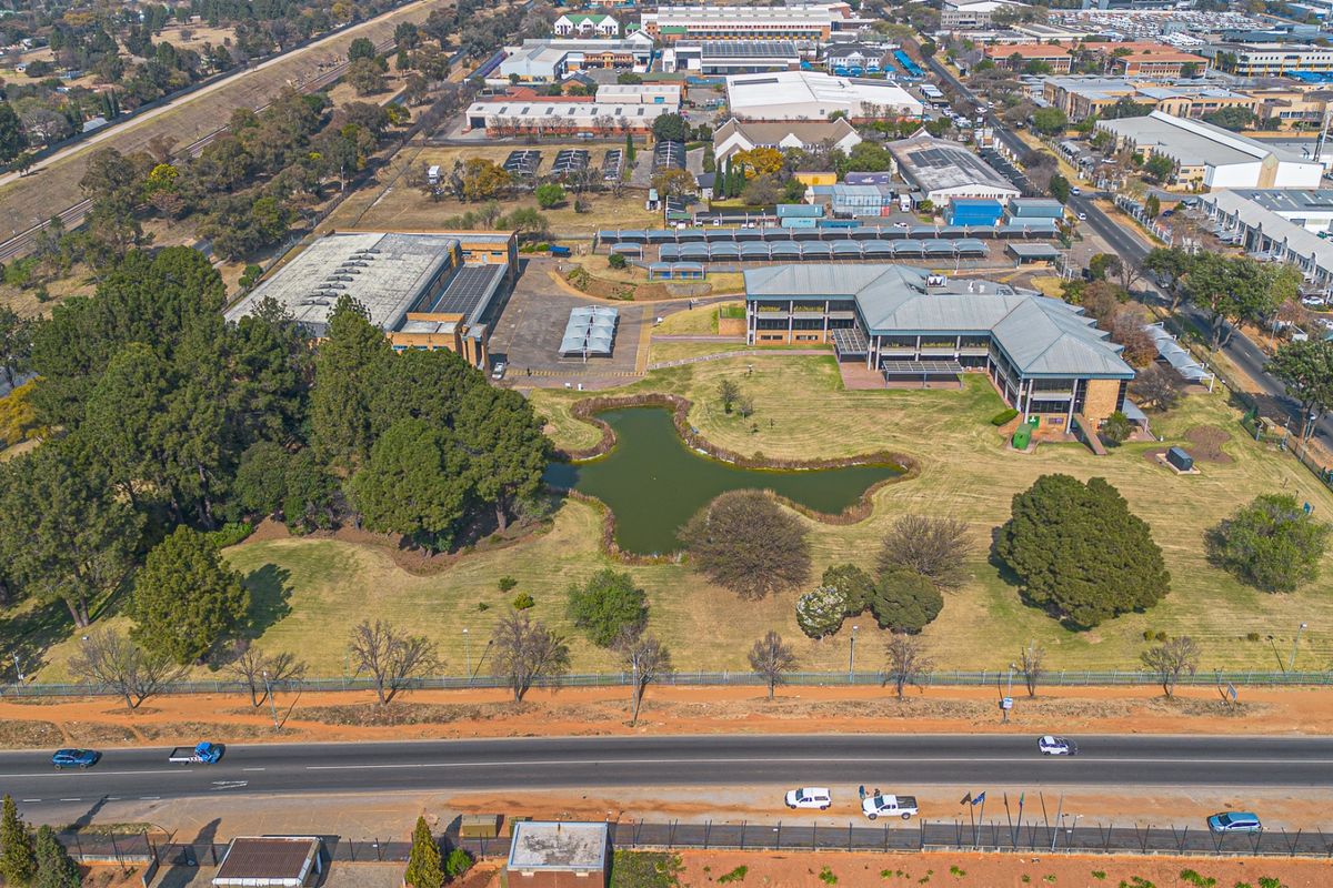 Aerial view of a commercial property complex featuring multiple office buildings, extensive landscaped grounds, a central pond, and ample paved parking facilities.