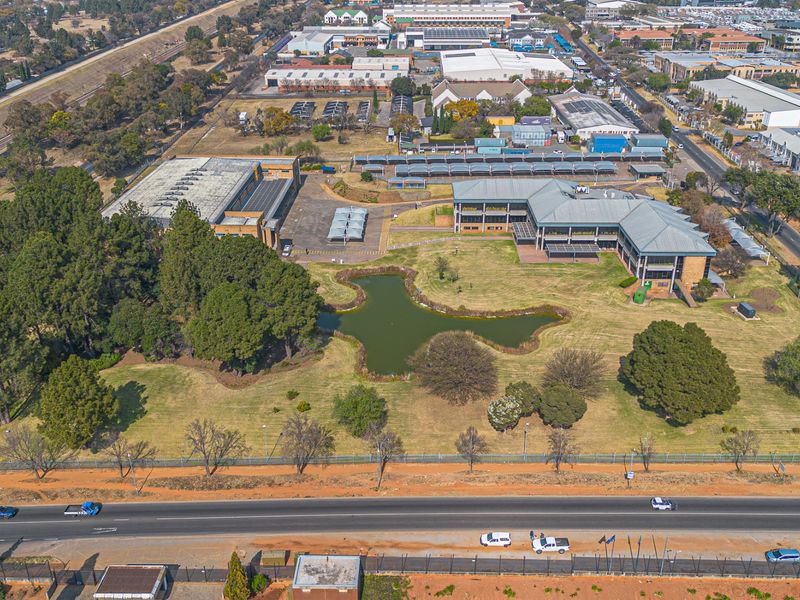 Aerial view of a commercial property complex featuring multiple office buildings, extensive landscaped grounds, a central pond, and ample paved parking facilities.