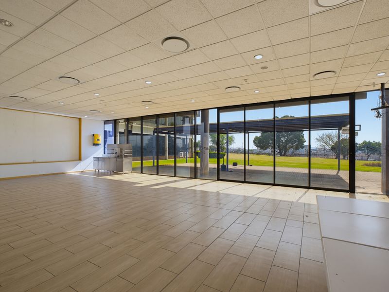 Spacious open-plan commercial area featuring large floor-to-ceiling glass doors, tiled flooring, and a suspended ceiling with recessed lighting, offering excellent natural light.