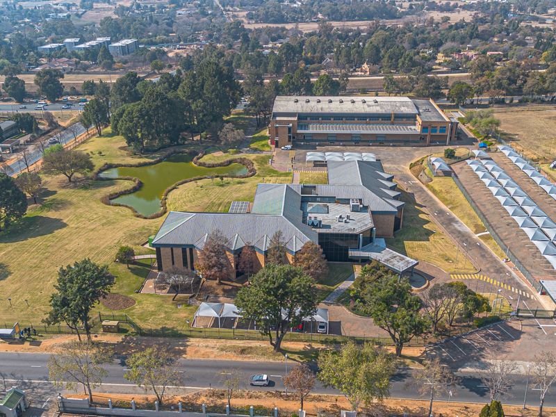 Aerial view of a commercial property featuring extensive landscaped grounds, a pond, multiple buildings with metal roofing, and a large shaded parking area.