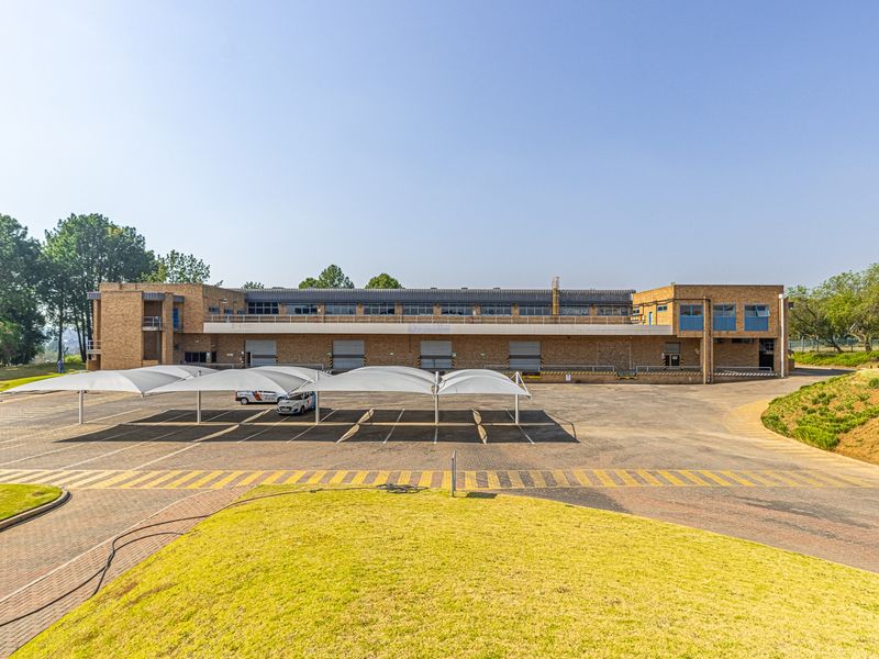 A wide-angle view of a commercial property featuring a brick facade, multiple roller shutter doors, and covered parking bays on a paved lot.