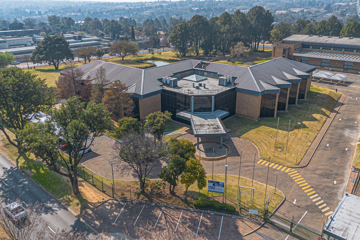 Aerial view of a commercial office complex featuring a paved driveway, extensive landscaped grounds, and secure perimeter fencing.