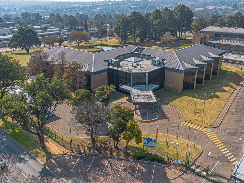 Aerial view of a commercial office complex featuring a paved driveway, extensive landscaped grounds, and secure perimeter fencing.