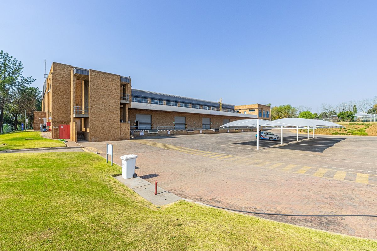 Rear view of a commercial industrial property featuring a paved yard, multiple loading bays with roller shutter doors, and covered parking structures.