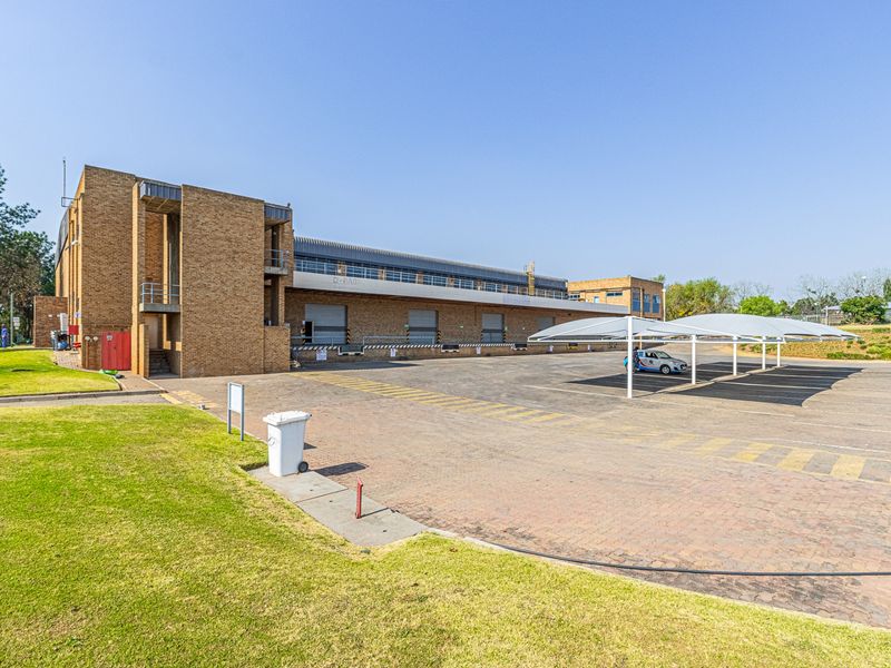 Rear view of a commercial industrial property featuring a paved yard, multiple loading bays with roller shutter doors, and covered parking structures.