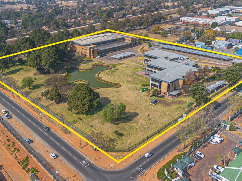 Aerial view of a large commercial property featuring multiple office buildings, extensive landscaped grounds, a central pond, and ample paved parking facilities.