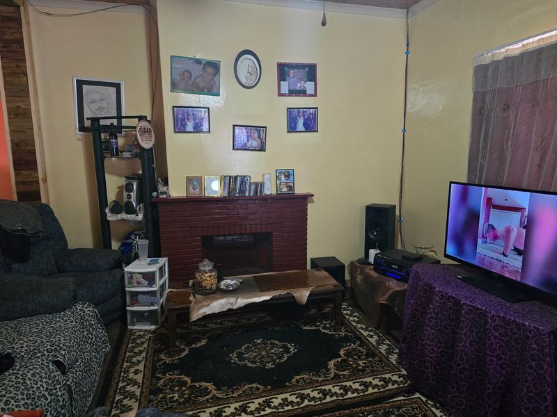 A living room featuring a traditional brick fireplace, currently used as a casual lounge area with visible wall finishes and electrical wiring.