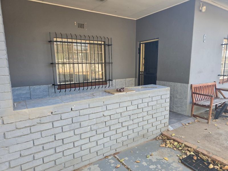 A covered patio area featuring a brick built-in counter with tiled surface, security window bars, and a security gate entrance.