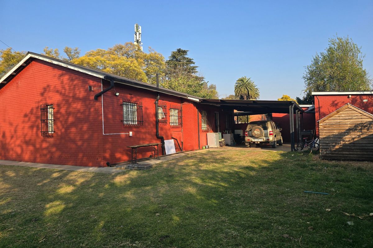 Rear view of the property featuring a red brick facade, security bars on windows, and a covered carport area with a spacious garden.