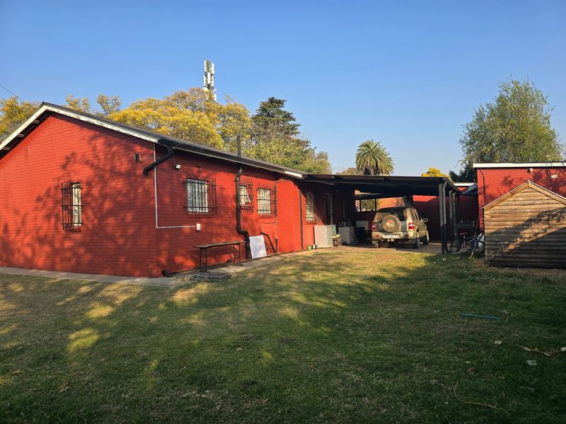Rear view of the property featuring a red brick facade, security bars on windows, and a covered carport area with a spacious garden.