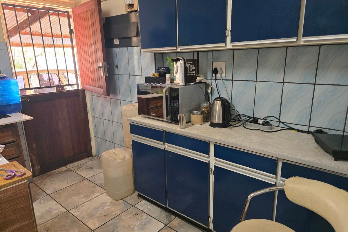A functional kitchen area featuring blue cabinetry, tiled splashbacks, and direct access to the exterior via a timber door with a security gate.