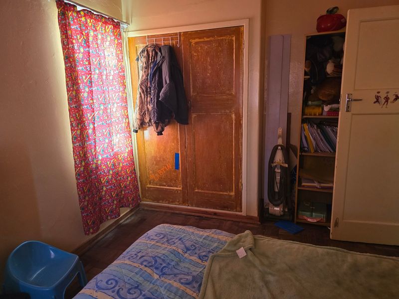 A bedroom featuring original wooden flooring and a built-in wooden wardrobe, requiring cosmetic updates to improve the overall aesthetic and condition.