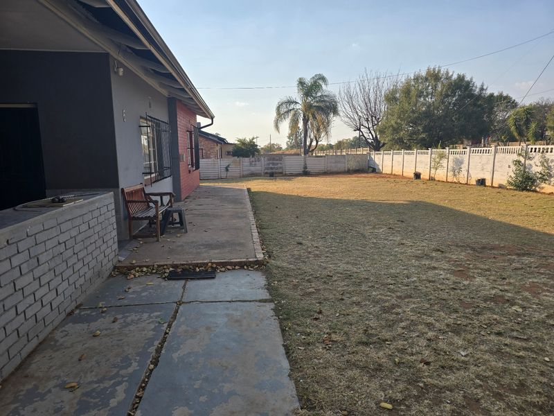 Spacious rear garden featuring a concrete patio area, built-in braai, and perimeter boundary walling.