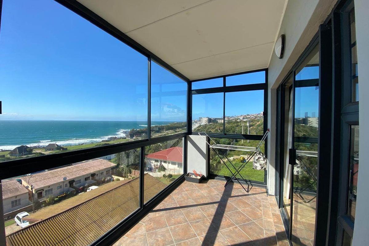 Enclosed balcony featuring tiled flooring and expansive glass windows offering panoramic coastal and ocean views.