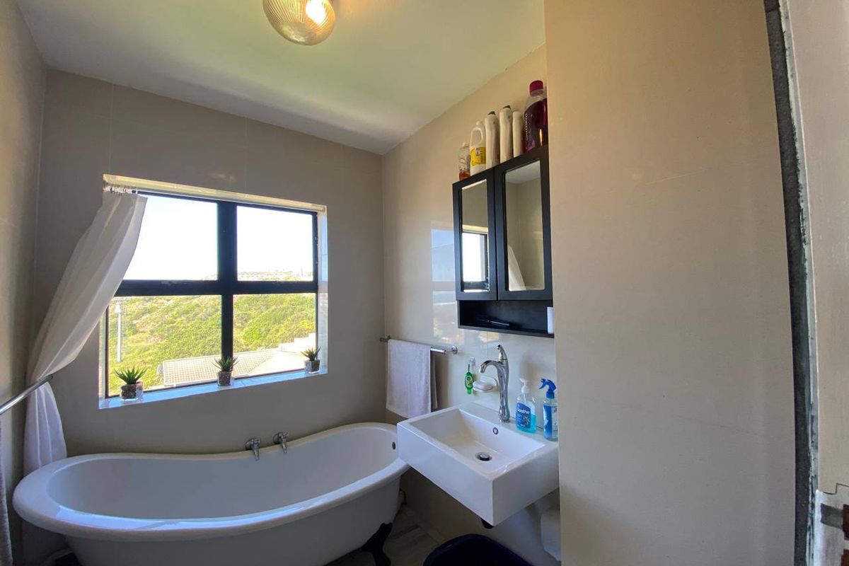 A bathroom featuring a freestanding bathtub, wall-mounted basin, and medicine cabinet, with natural light provided by a window overlooking the exterior.