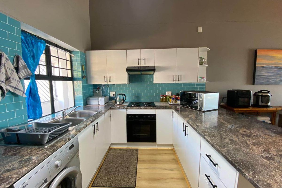 Functional kitchen featuring white cabinetry, granite-look laminate countertops, teal subway tile backsplash, and integrated appliances including an oven and hob.