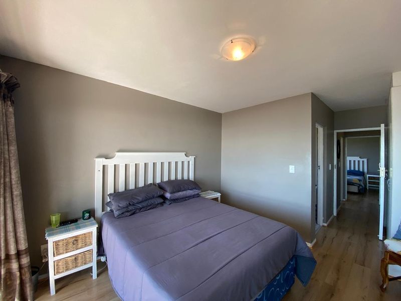 A bedroom featuring laminate flooring and neutral wall tones, with a view leading into an adjacent room.