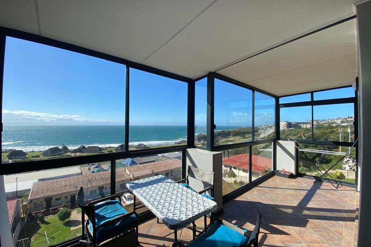 An enclosed balcony featuring tiled flooring and expansive aluminum-framed windows offering panoramic coastal and ocean views.