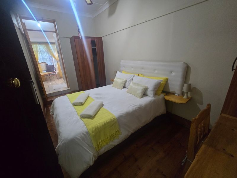A bedroom featuring hardwood flooring, a ceiling fan, and a picture rail, with an adjoining space visible through the doorway.