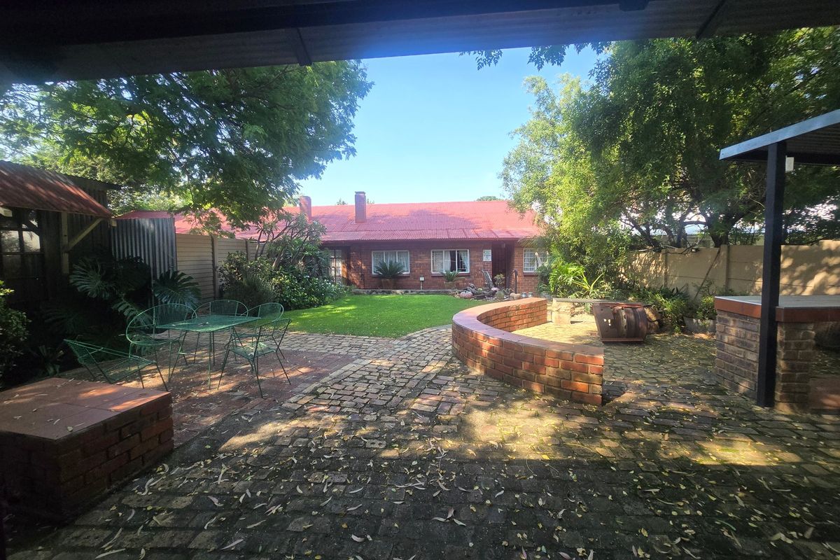 A spacious rear garden featuring brick paving, a built-in braai area, a low brick retaining wall, and a well-maintained lawn.