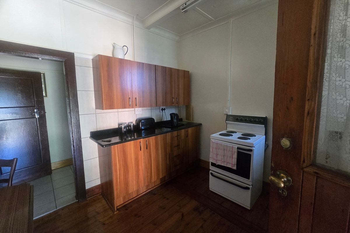A compact kitchen featuring wooden cabinetry, stone countertops, a tiled splashback, and a freestanding electric stove, set against timber flooring.