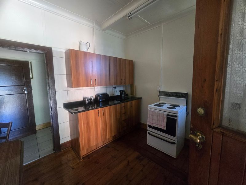 A compact kitchen featuring wooden cabinetry, stone countertops, a tiled splashback, and a freestanding electric stove, set against timber flooring.