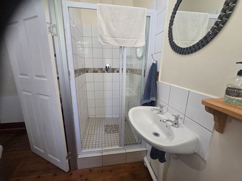 A functional bathroom featuring a tiled shower enclosure and a wall-mounted basin with classic chrome taps, complemented by timber flooring.