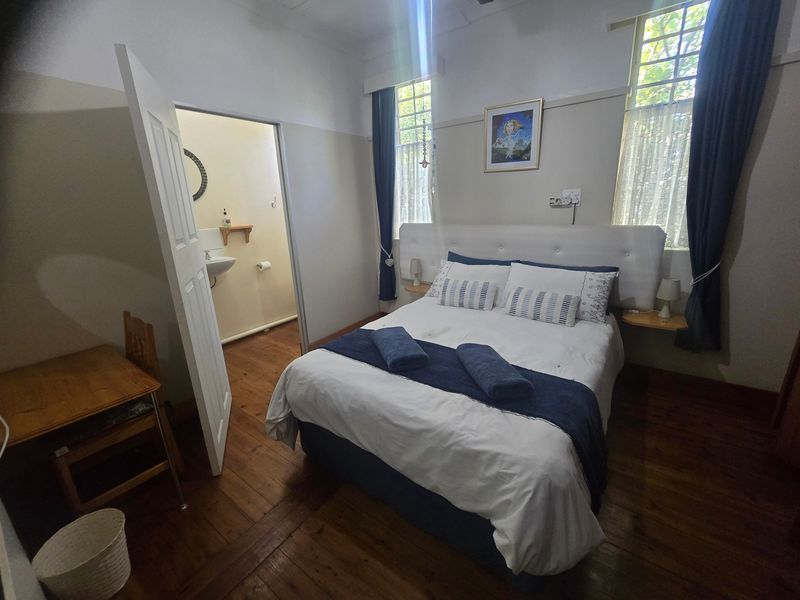 A cozy bedroom featuring original hardwood flooring, classic picture rails, and sash windows, with an adjoining en-suite bathroom.