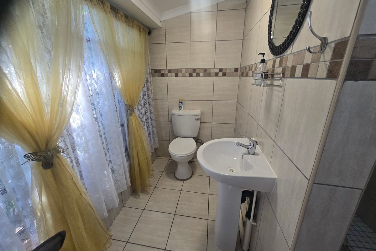A functional bathroom featuring tiled walls and flooring, a pedestal basin, and a standard toilet, with natural light provided by a large window.