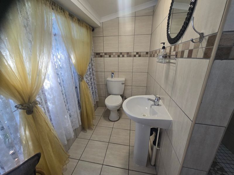 A functional bathroom featuring tiled walls and flooring, a pedestal basin, and a standard toilet, with natural light provided by a large window.