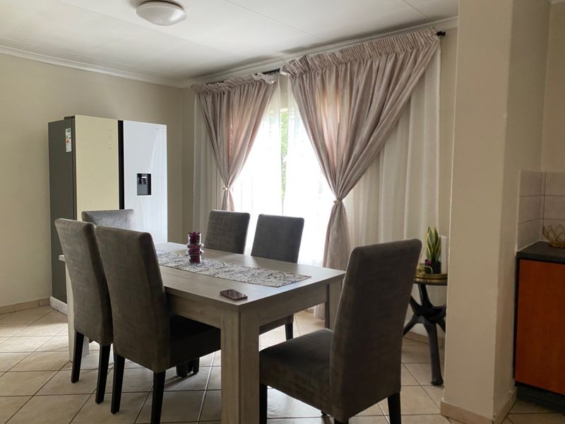 A functional dining area featuring tiled flooring and natural light through window curtains, adjacent to a kitchen space.