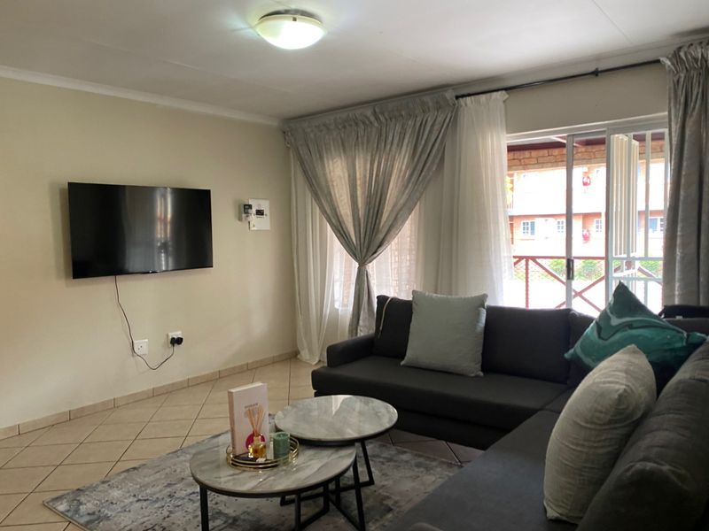 A comfortable living room featuring tiled flooring, a ceiling light fixture, and a sliding glass door providing access to the outdoor area.