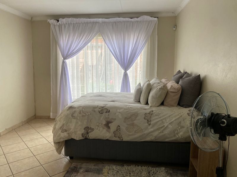 A functional bedroom featuring tiled flooring and large windows with curtain rails, providing a neutral base for personalization.