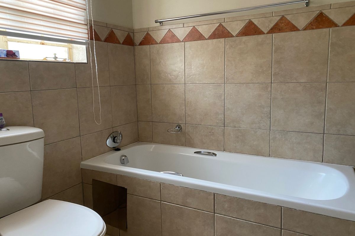 A functional bathroom featuring a built-in bathtub with tiled surround, a toilet, and decorative border tiles.